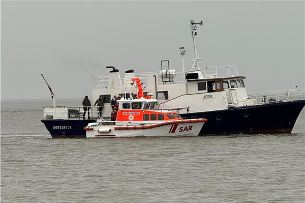 Mit dem Seenotrettungsboot Wilma Sikorski der DGzRS übernehmen die Seenotretter acht Menschen von einem festgekommenen Bestattungsschiff.